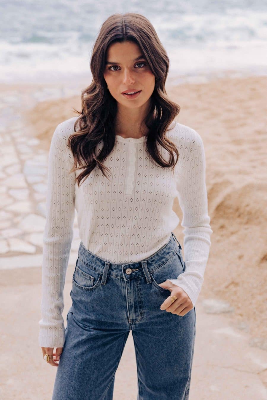 Top Elowan Sahoma blanc en maille ajourée et col tunisien, manches longues, portée avec un jean bleu foncé