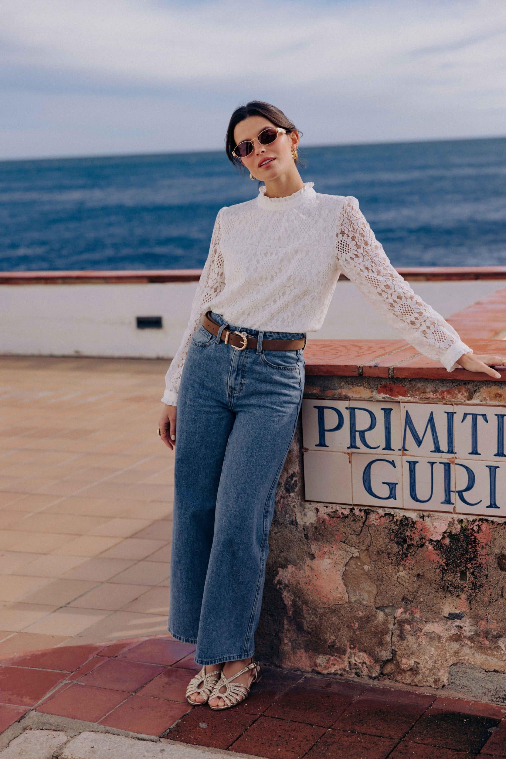 blouse-leona-blanche-sahoma-00003 Blouse Leona Sahoma blanche aux motifs floraux en dentelle, col montant à volants, manches longues, portée avec un jean bleu foncé