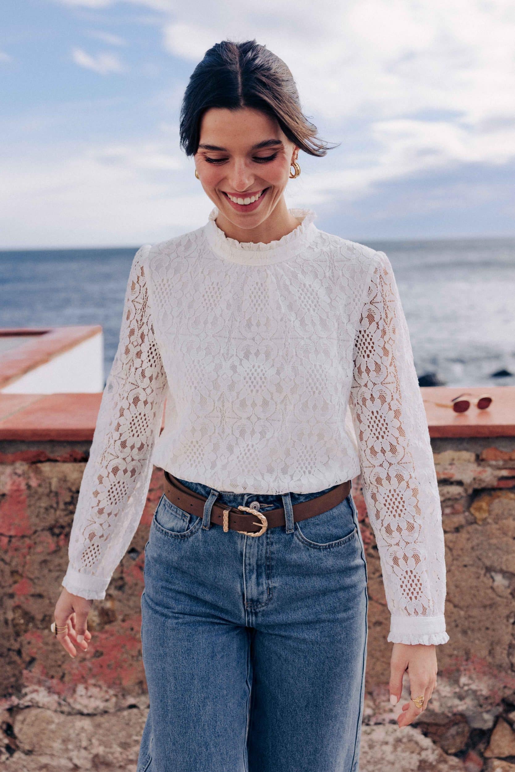 blouse-leona-blanche-sahoma-00009 Blouse Leona Sahoma blanche aux motifs floraux en dentelle, col montant à volants, manches longues, portée avec un jean bleu foncé