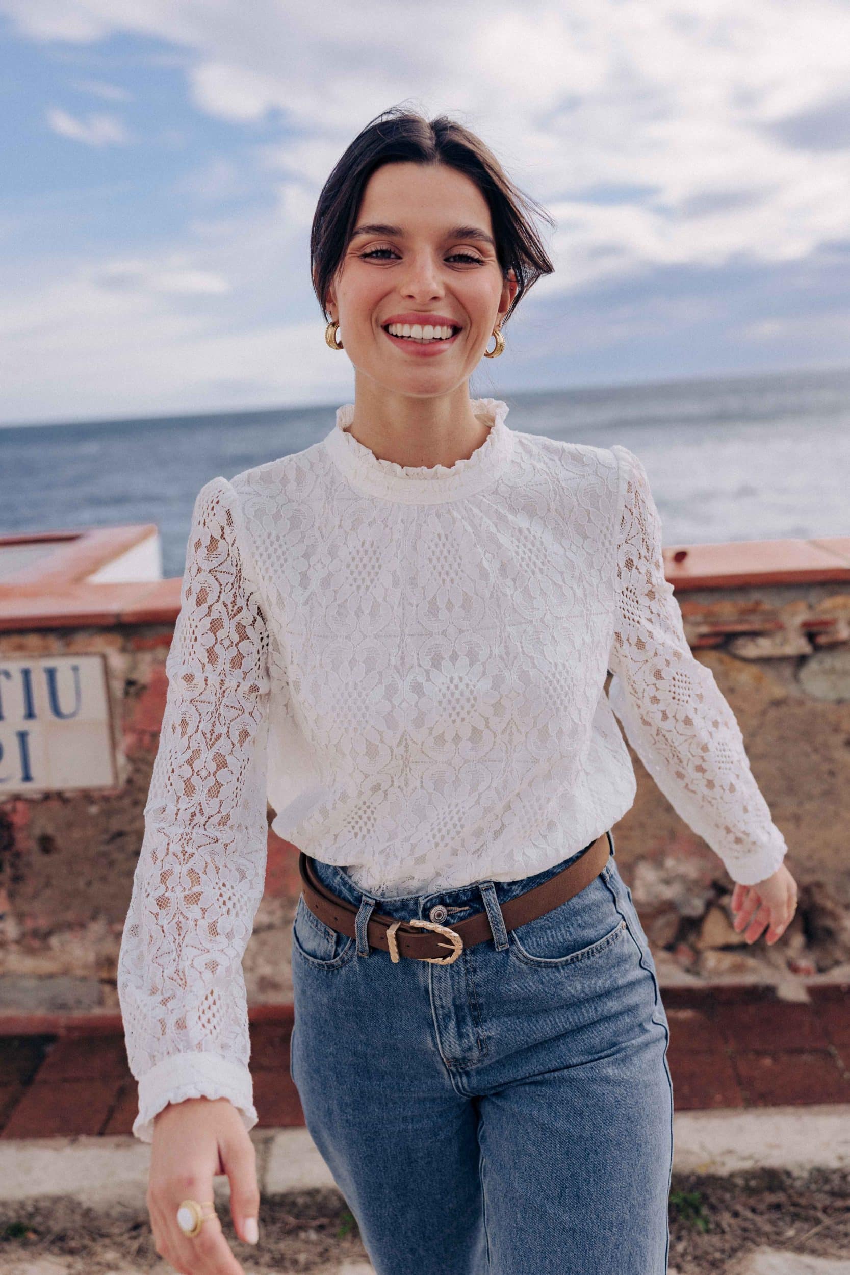 blouse-leona-blanche-sahoma-00010 Blouse Leona Sahoma blanche aux motifs floraux en dentelle, col montant à volants, manches longues, portée avec un jean bleu foncé
