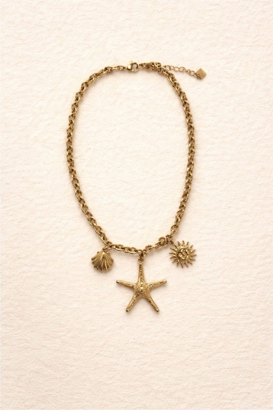 Collier El Mar doré porté autour du cou, avec breloques soleil, étoile de mer et coquillage, esprit marin et estival.