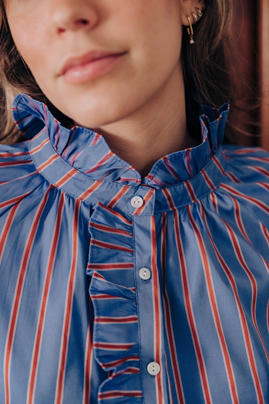Blouse Naïra Sahoma bleue à rayures rouges avec jabot et col montant à volants, portée avec le jean Omar gris