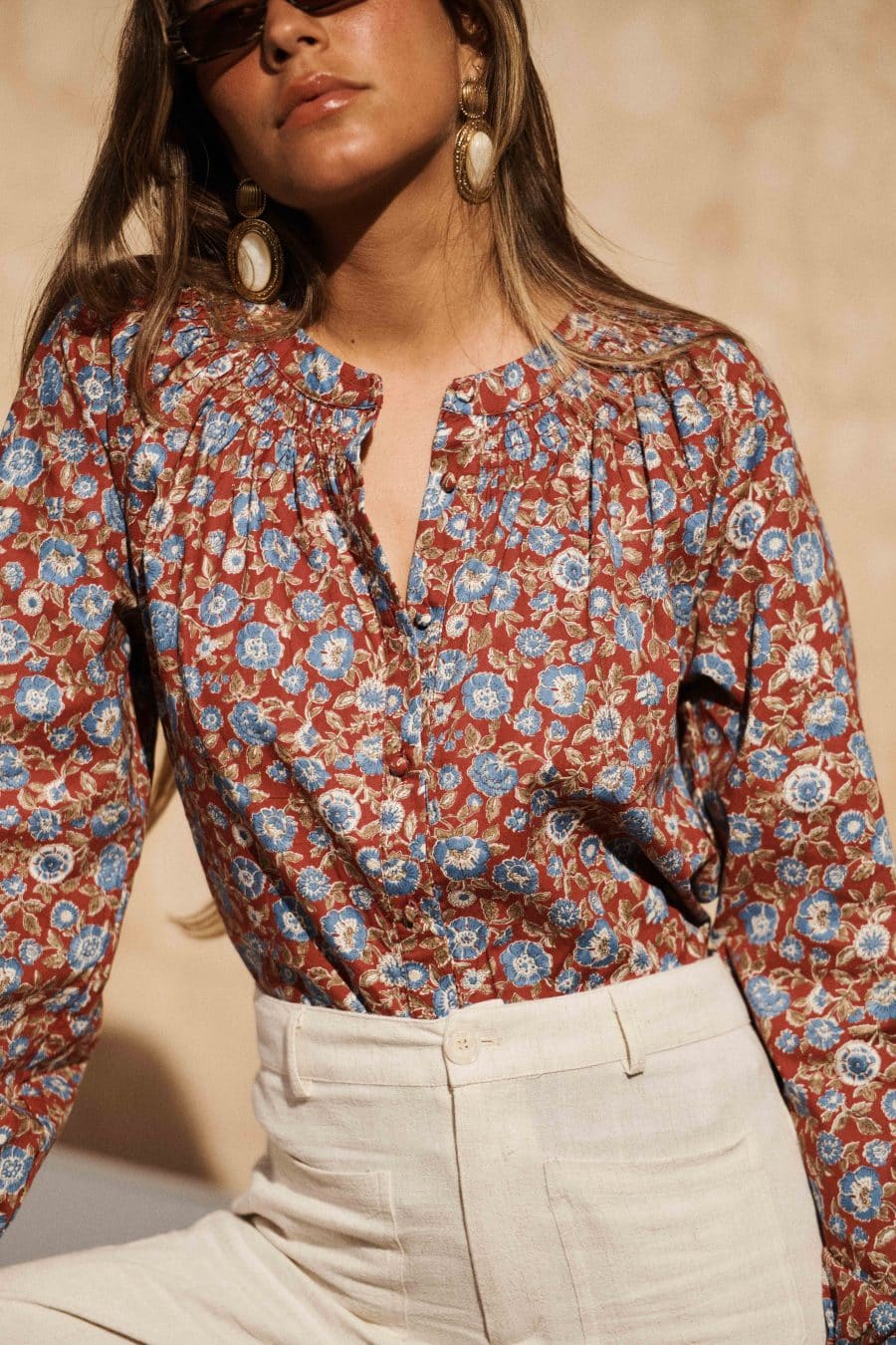 Blouse Coline Sahoma Rouge bordeaux à motifs floraux bleus, manches longues, portée avec un pantalon léger clair