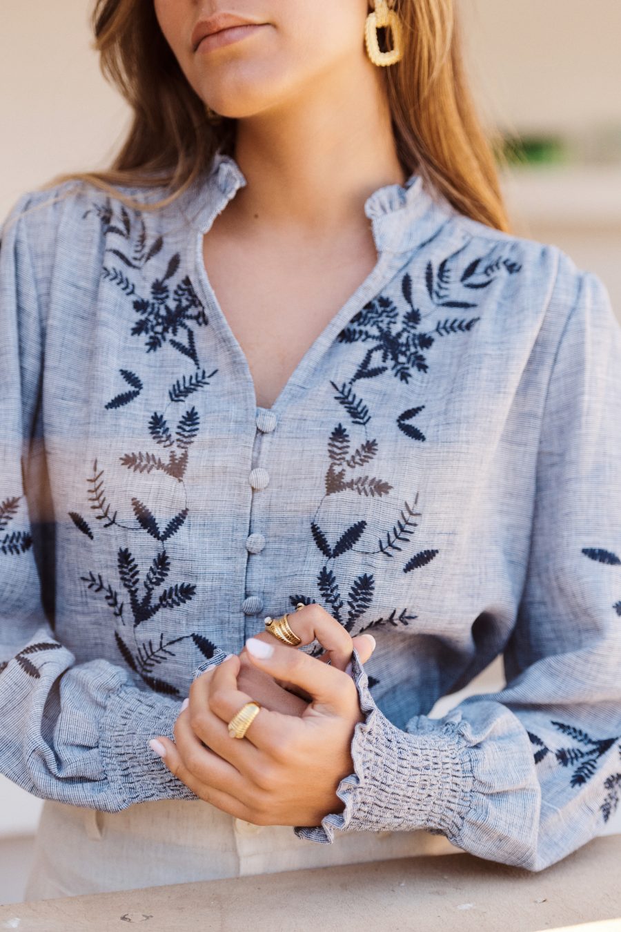 Blouse Nellie Sahoma bleue broderie à motifs floraux, manches longues, portée avec un pantalon clair