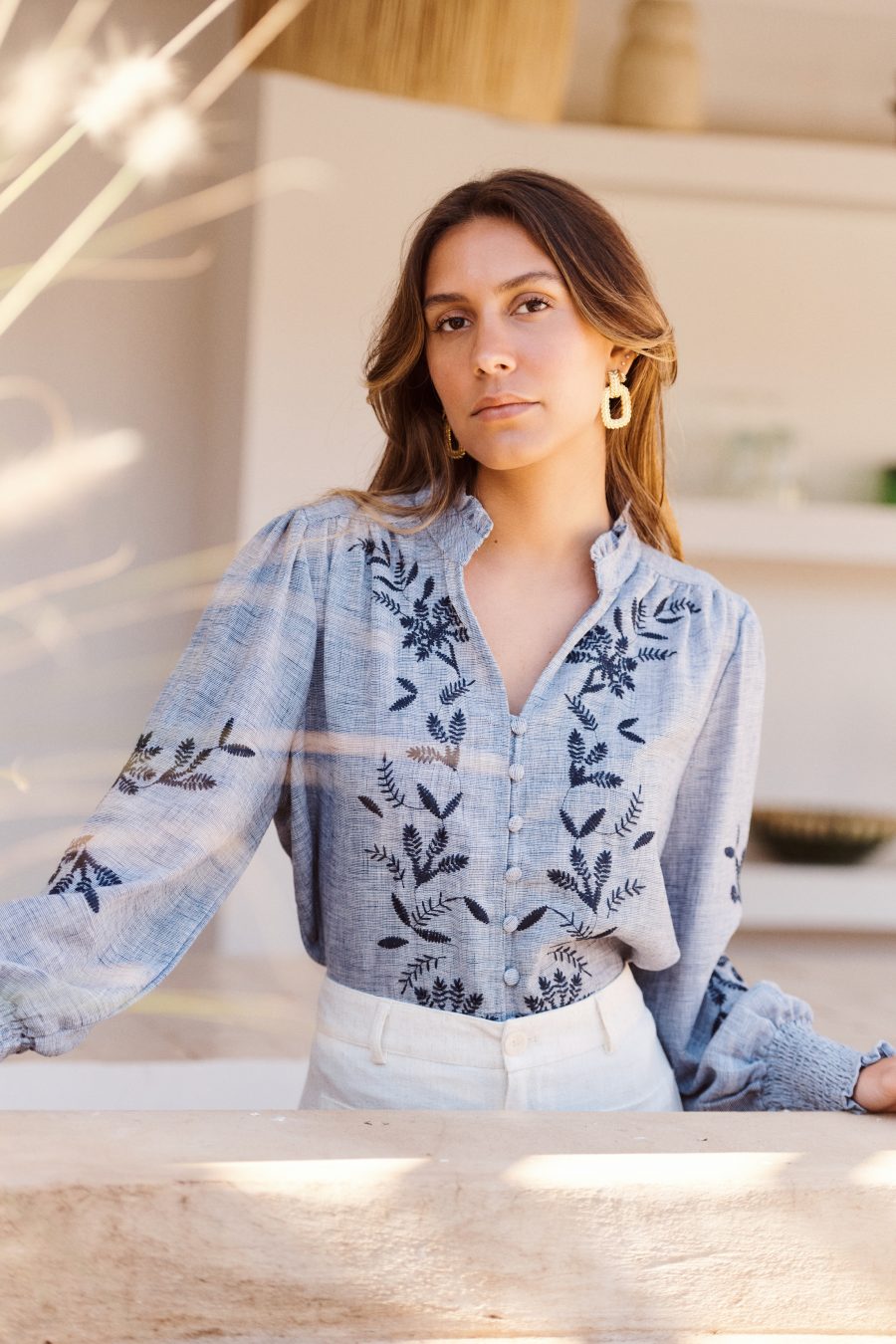 Blouse Nellie Sahoma bleue broderie à motifs floraux, manches longues, portée avec un pantalon clair