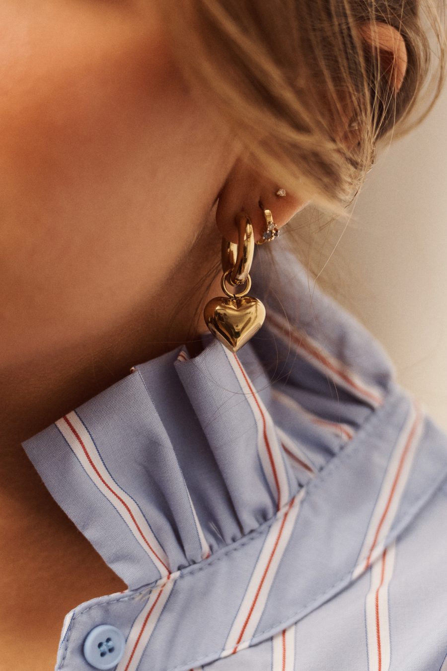 Boucles d'oreilles Romane Sahoma dorées ornée d'un pendentif forme coeur, portée en accumulation