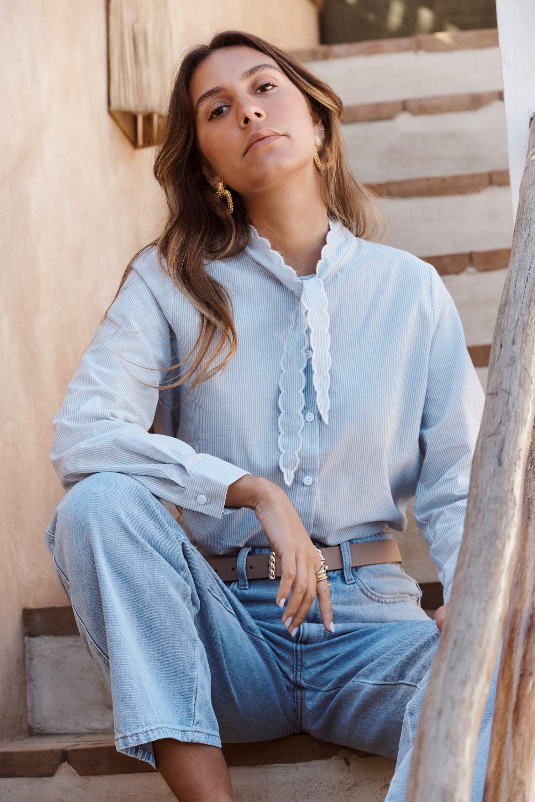 Chemise Sibel Sahoma rayée bleue à col lavallière ondulé et délicat, manches longues, portée avec un jean clair
