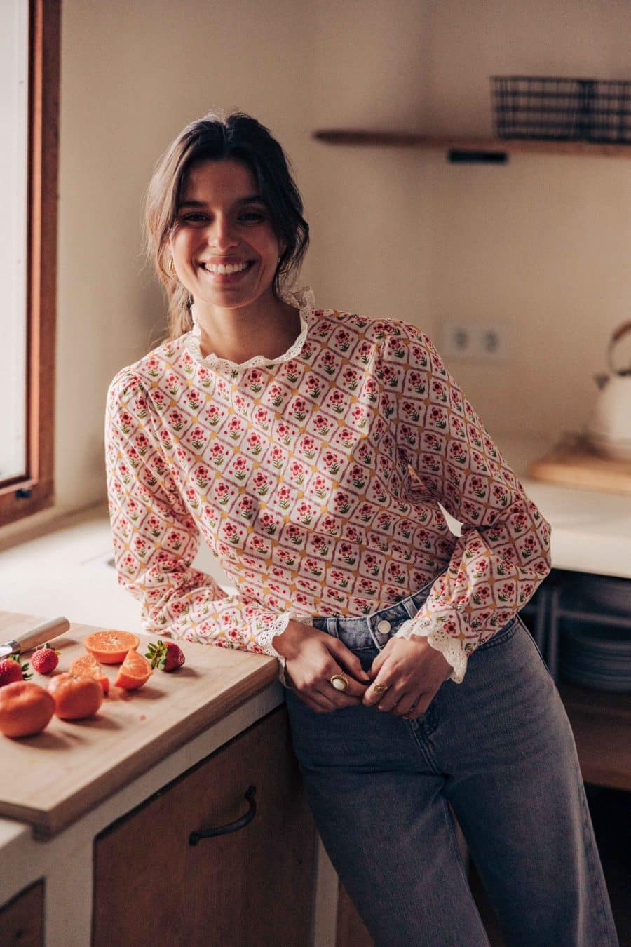 Blouse Niam Sahoma écrue aux motifs floraux colorés, col montant à volants, manches longues, portée avec un jean gris clair