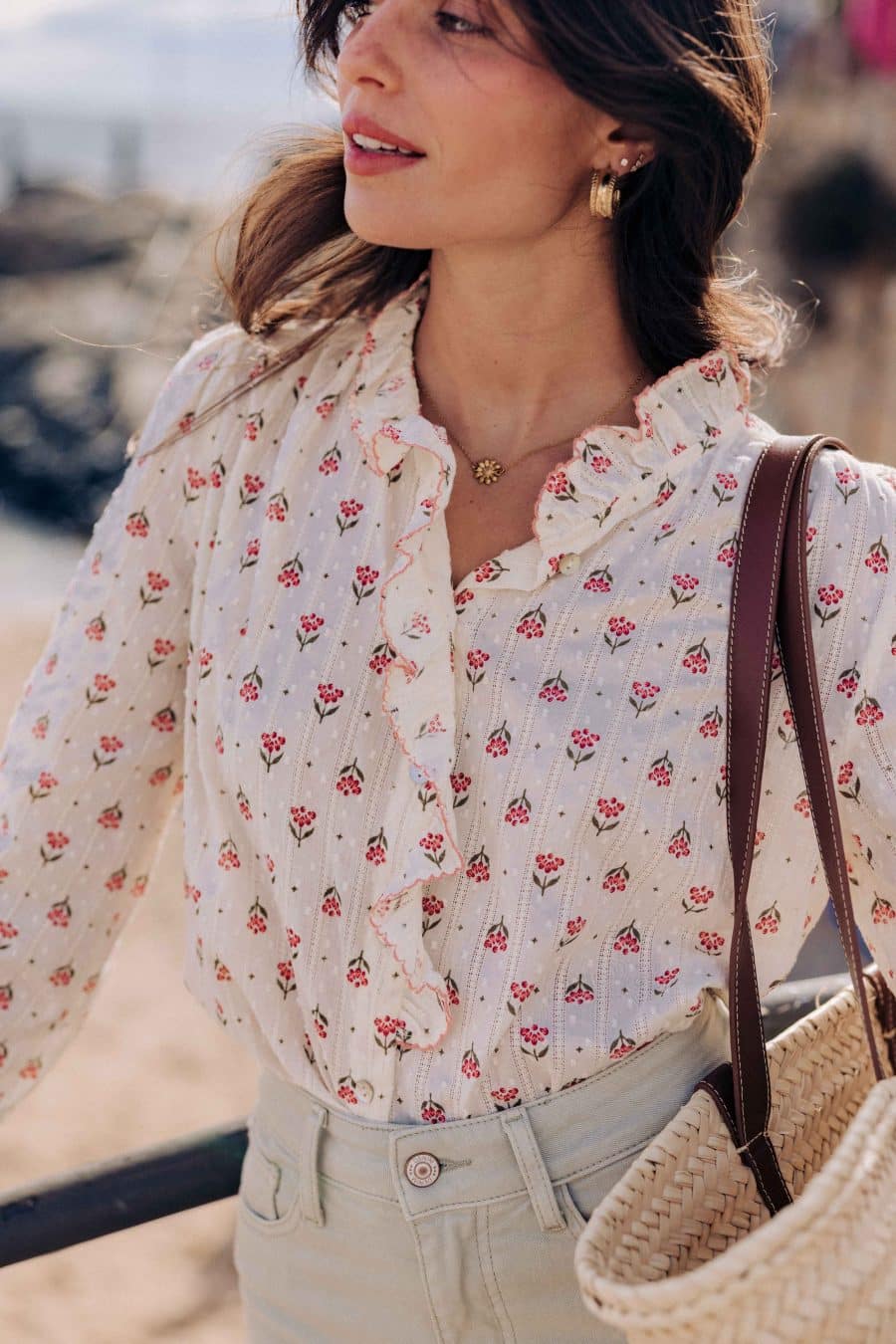 Chemise Eilis Sahoma écrue aux motifs floraux rose, col montant à volants et jabot, manches longues, portée avec un jean vert d'eau