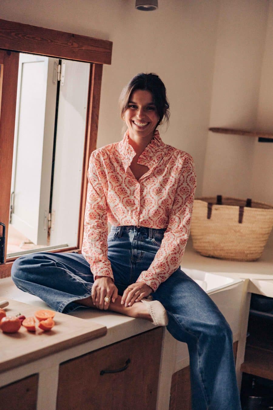 Chemise Maeline Sahoma écrue aux motifs floraux orangés, col montant à volants, manches longues, portée avec un jean bleu foncé