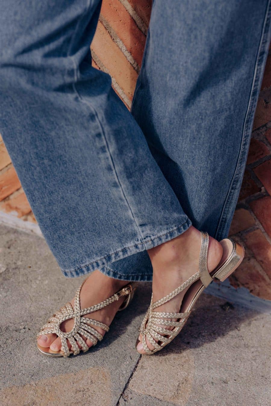 Sandales Auréa Sahoma dorées à brides croisées, semelles plates avec talon de 2,5cm de hauteur, portées avec un jean