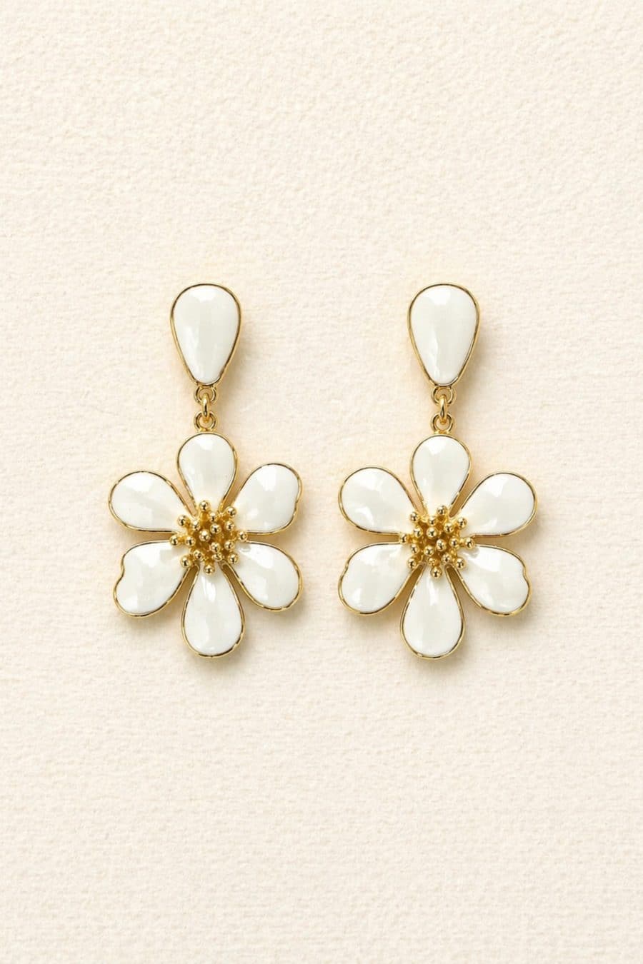 Boucles d’oreilles blanches et dorées, forme fleur en relief, posées sur fond blanc