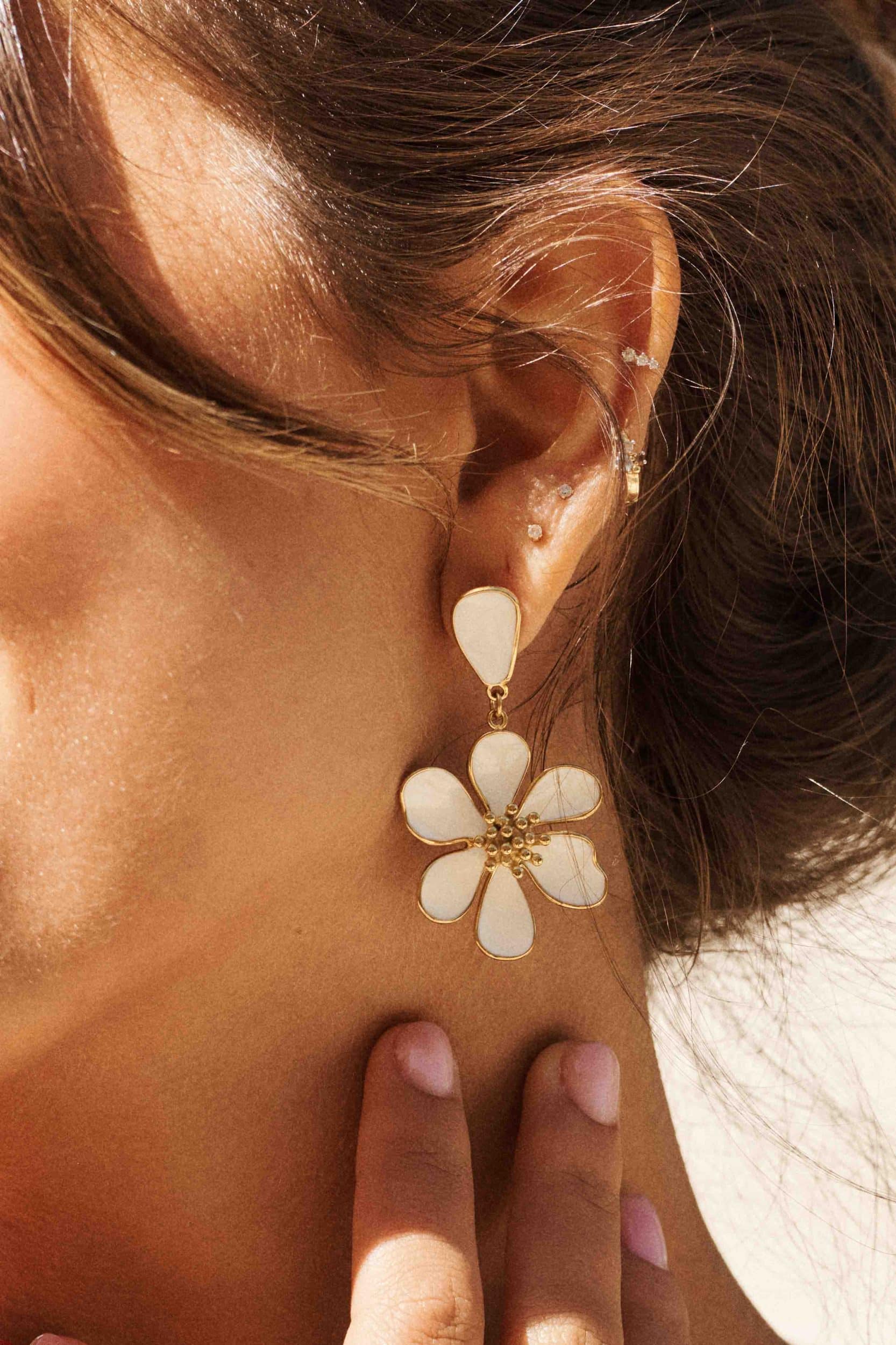 Boucles d’oreilles blanches et dorées, forme fleur en relief, posées sur fond blanc